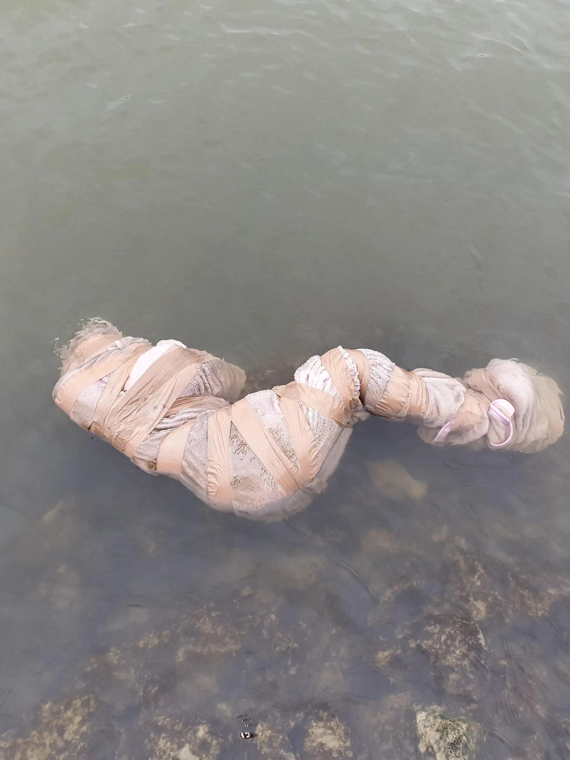 HANDOUT - 26.01.2019, Nordrhein-Westfalen, Marl: Eine in eine Decke gewickelte und mit Klebeband verschnürte, lebensecht wirkende Puppe liegt im Wesel-Datteln-Kanal. Eine Spaziergängerin hatte den makaberen Fund gemacht und die Polizei alarmiert. Als die Rettungskräfte das Paket öffneten, kam die rund 1,50 Meter große Kunststoffpuppe zum Vorschein. (zu dpa «Verschnürte Puppe treibt wie Wasserleiche in Kanal» vom 26.02.2019) Foto: -/Feuerwehr Marl/dpa - ACHTUNG: Nur zur redaktionellen Verwendung und nur mit vollständiger Nennung des vorstehenden Credits +++ dpa-Bildfunk +++
