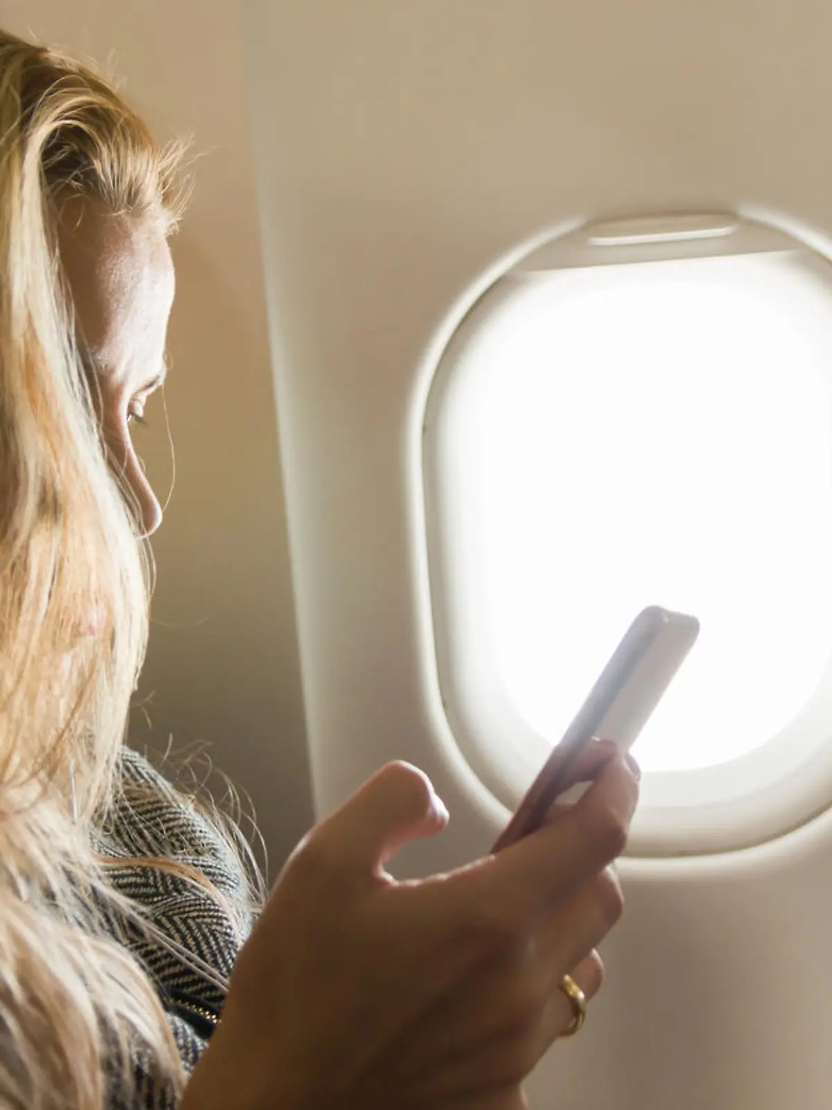Frau sitzt mit ihrem Handy im Flugzeug.