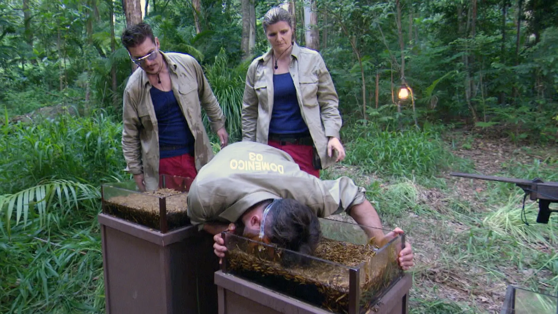 Tag 1 - Dschungelprüfung "Starschuss". V.l.: Chris Töpperwien, Domenico de Cicco und Sandra Kiriasis müssen auf dem Weg ins Camp noch eine Dschungelprüfung bestehen. Aus Behältern voller Kakerlaken, Maden und Schleim müssen sie mit ihren Mündern jeweils einen Ball fischen. Die erkämpften Bälle dienen dann als Munition für eine Armbrust. Für jeden Treffer auf Tierschilder in einem Baum gibt es einen Stern.