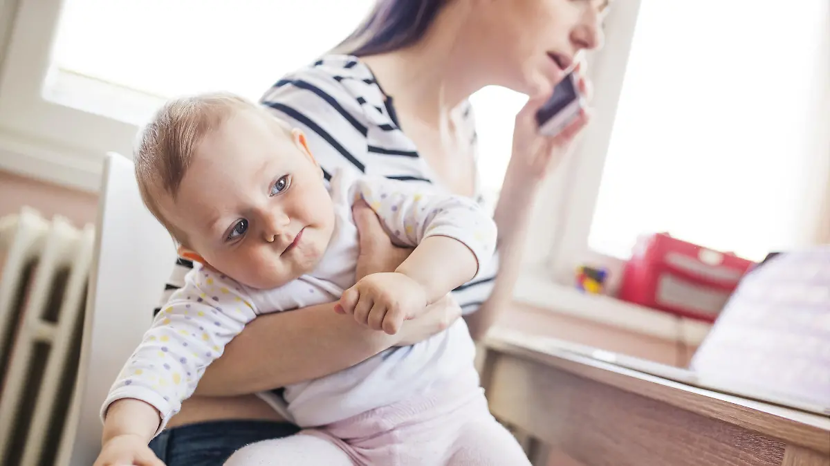 Junge Mutter telefoniert mit Kleinkind auf dem Arm.