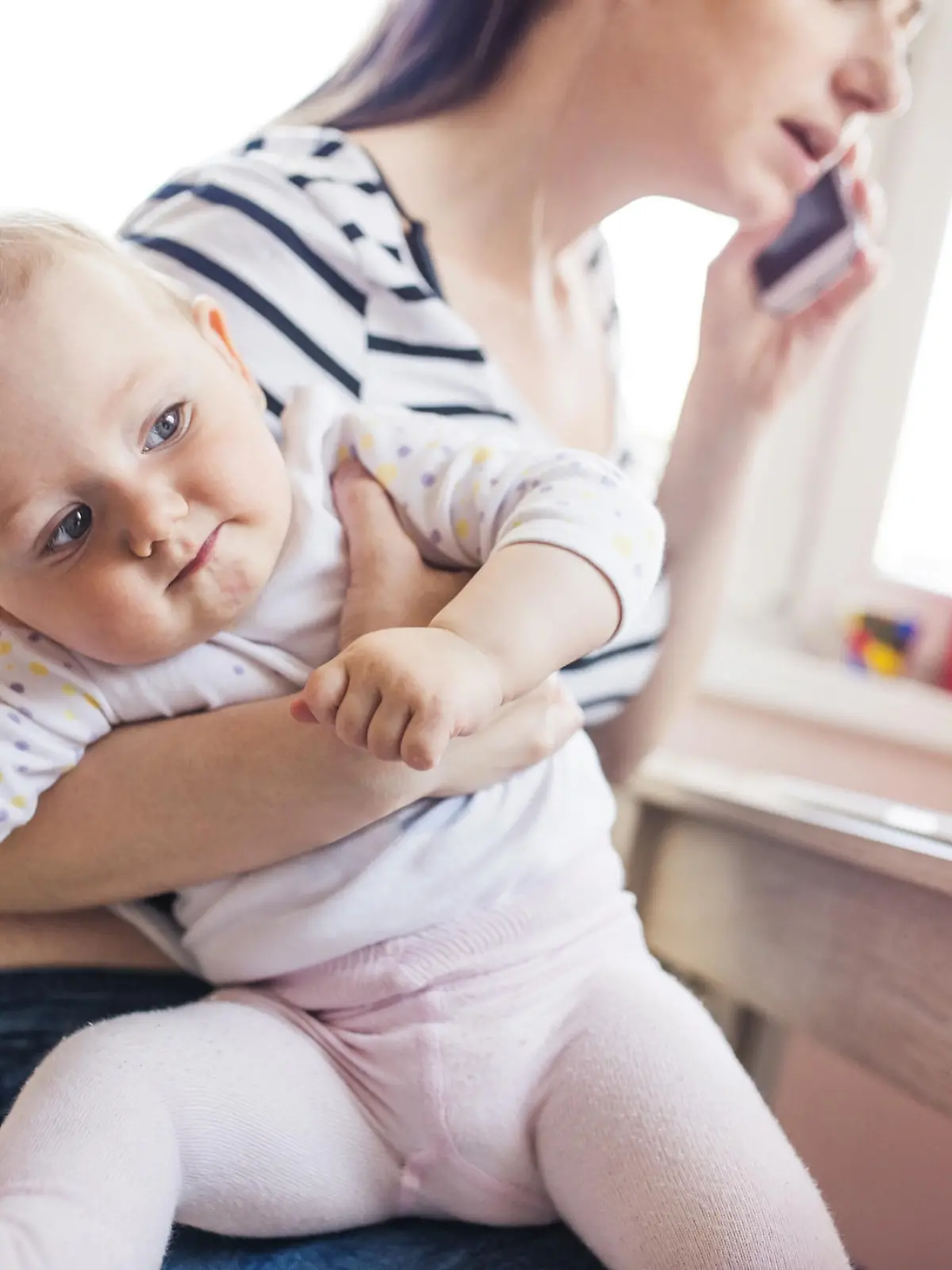 Junge Mutter telefoniert mit Kleinkind auf dem Arm.