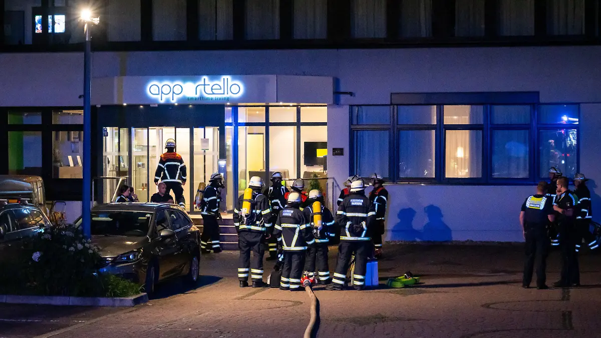 14.08.2023, Hamburg: Einsatzkräfte von Feuerwehr und Polizei stehen vor einem Hotel. Vor einem Hotel in Hamburg, in dem hauptsächlich ukrainische Flüchtlinge untergebracht sind, haben Müllcontainer und der dazugehörige Unterstand gebrannt. Foto: Jonas Walzberg/dpa +++ dpa-Bildfunk +++