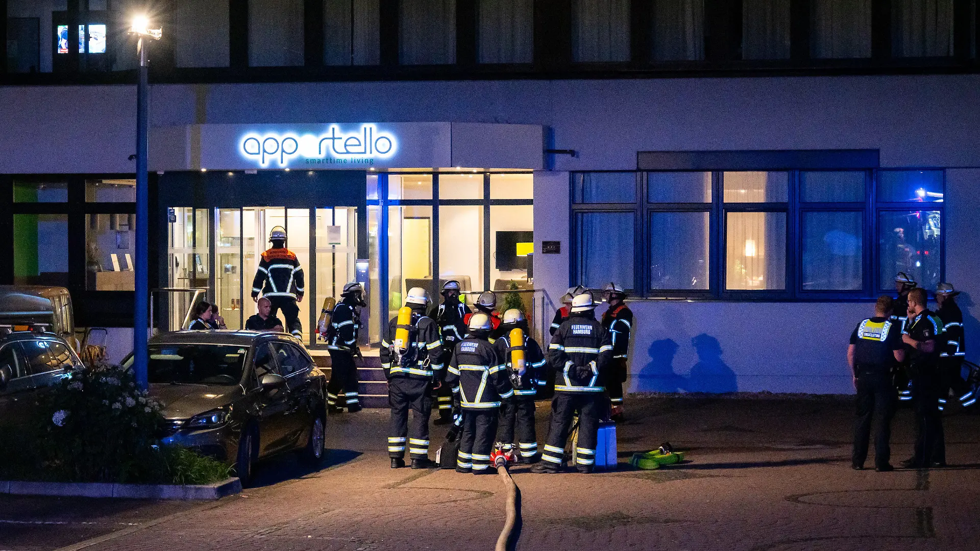 14.08.2023, Hamburg: Einsatzkräfte von Feuerwehr und Polizei stehen vor einem Hotel. Vor einem Hotel in Hamburg, in dem hauptsächlich ukrainische Flüchtlinge untergebracht sind, haben Müllcontainer und der dazugehörige Unterstand gebrannt. Foto: Jonas Walzberg/dpa +++ dpa-Bildfunk +++
