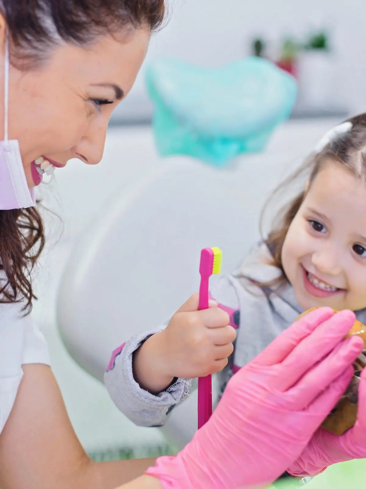 Smiling girl sitting in dentist chair with her pediatric dentist showing her teeth model and teaching her how to brush teeth. Dentistry, oral hygiene concept