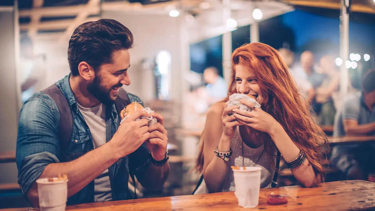 A young couple having snack and drink at an outdoors music festival. Eating burgers with fries and drinking beer.