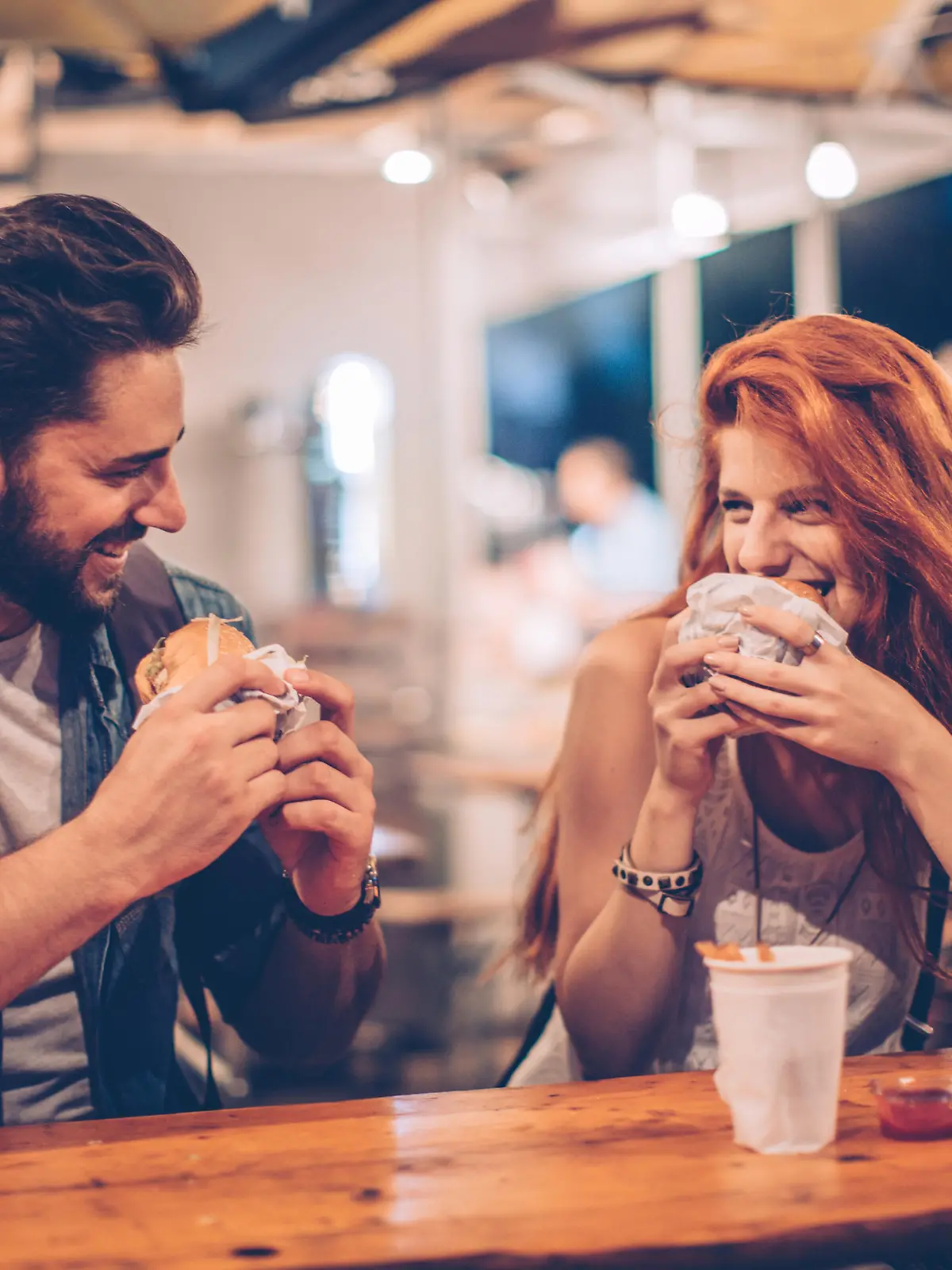 A young couple having snack and drink at an outdoors music festival. Eating burgers with fries and drinking beer.