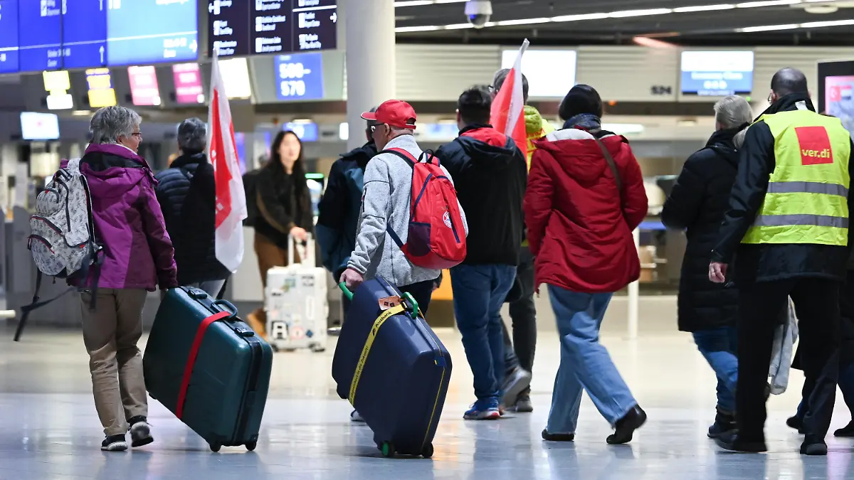 17.02.2023, Hessen, Frankfurt/Main: Ein älteres Paar aus Frankfurt, das eigentlich nach Fuerteventura fliegen wollte, läuft suchend neben streikenden Flughafen-Mitarbeitern durch Abflughalle B im Terminal 1 des Frankfurter Flughafens. Die Gewerkschaft Verdi hatte angekündigt, in der Tarifauseinandersetzung im öffentlichen Dienst am Freitag sieben Flughäfen ganztägig lahmzulegen. Foto: Arne Dedert/dpa +++ dpa-Bildfunk +++