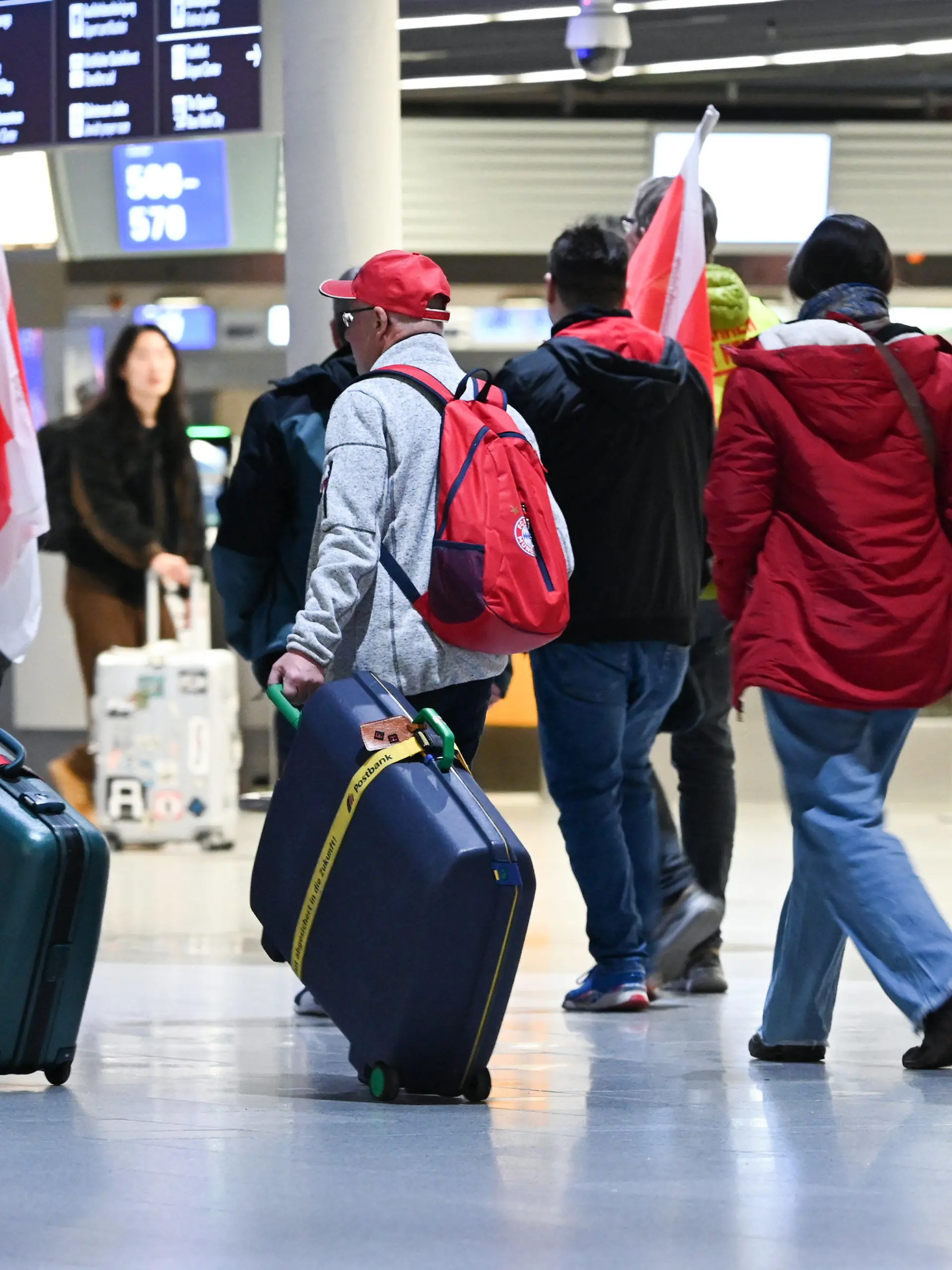 17.02.2023, Hessen, Frankfurt/Main: Ein älteres Paar aus Frankfurt, das eigentlich nach Fuerteventura fliegen wollte, läuft suchend neben streikenden Flughafen-Mitarbeitern durch Abflughalle B im Terminal 1 des Frankfurter Flughafens. Die Gewerkschaft Verdi hatte angekündigt, in der Tarifauseinandersetzung im öffentlichen Dienst am Freitag sieben Flughäfen ganztägig lahmzulegen. Foto: Arne Dedert/dpa +++ dpa-Bildfunk +++