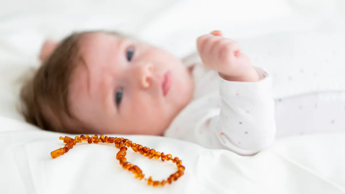 Baby liegt mit einer Bernsteinkette im bett.