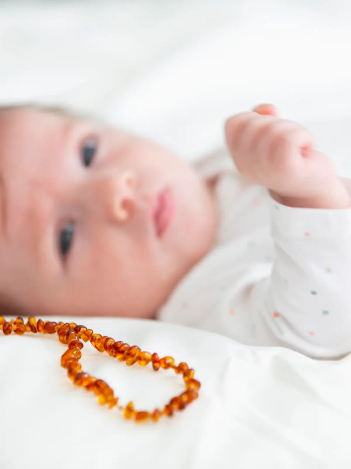 Baby liegt mit einer Bernsteinkette im bett.