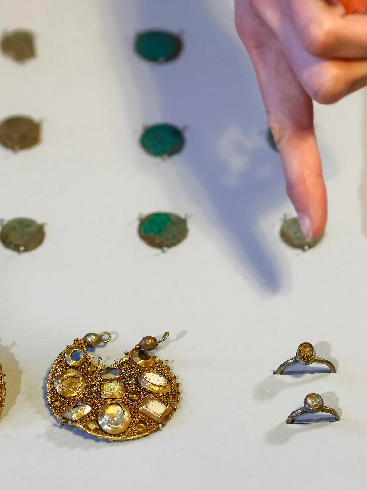 17.02.2023, Schleswig-Holstein, Schleswig: Eine Mitarbeiterin des Archäologischen Landesamtes Schleswig-Holstein deutet mit dem Finger auf zwei Ohranhänger. Mitarbeiter des Landesamtes hatten mit Hilfe von Detektoren den Schmuck aus der Zeit um 1100 gefunden. Laut Landesamt wurde der Schmuck vermutlich vor rund 800 Jahren von einem Reisenden versteckt. Foto: Frank Molter/dpa +++ dpa-Bildfunk +++