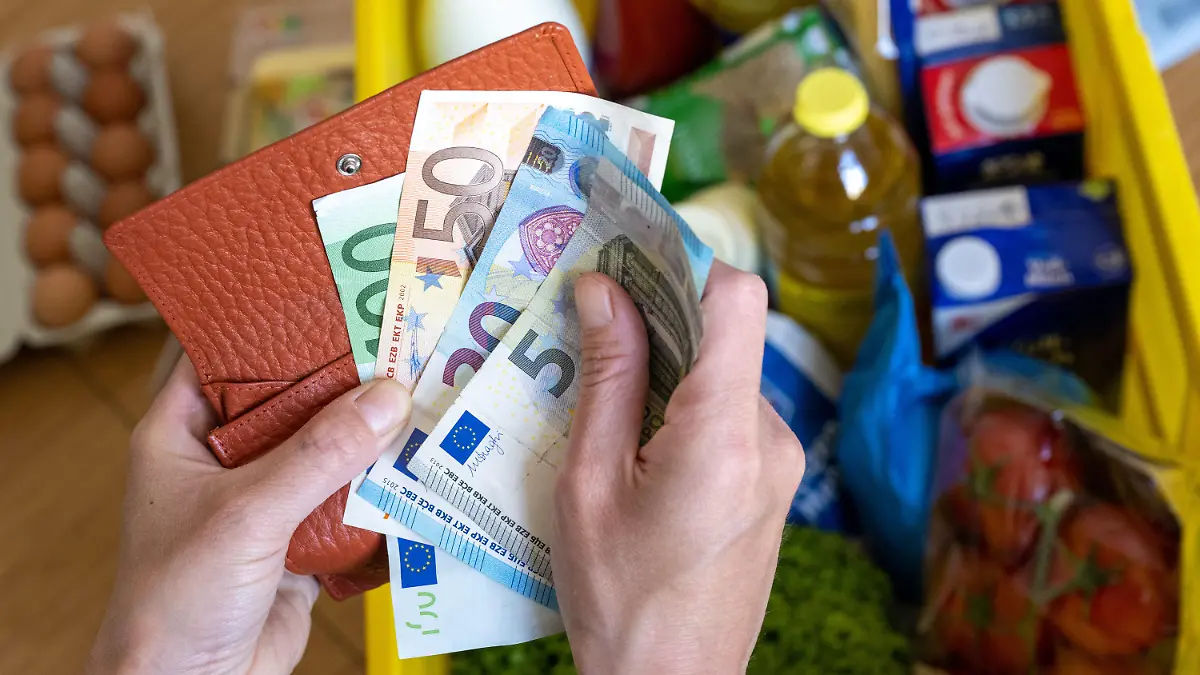 ARCHIV - 02.06.2022, Sachsen, Leipzig: Eine Einkaufskiste mit Lebensmitteln steht auf einem Küchentisch, während eine Frau Euro-Banknoten in den Händen hält. Die hohe Inflation bremst einer Umfrage zufolge viele Sparer in Deutschland aus. (zu dpa «Umfrage: Nur noch jeder Zweite kann aktuell noch sparen») Foto: Hendrik Schmidt/dpa +++ dpa-Bildfunk +++