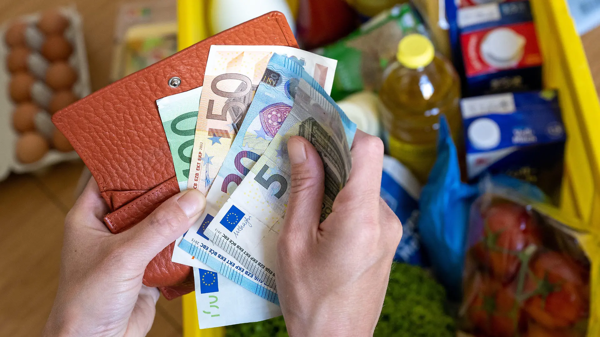 ARCHIV - 02.06.2022, Sachsen, Leipzig: Eine Einkaufskiste mit Lebensmitteln steht auf einem Küchentisch, während eine Frau Euro-Banknoten in den Händen hält. Die hohe Inflation bremst einer Umfrage zufolge viele Sparer in Deutschland aus. (zu dpa «Umfrage: Nur noch jeder Zweite kann aktuell noch sparen») Foto: Hendrik Schmidt/dpa +++ dpa-Bildfunk +++