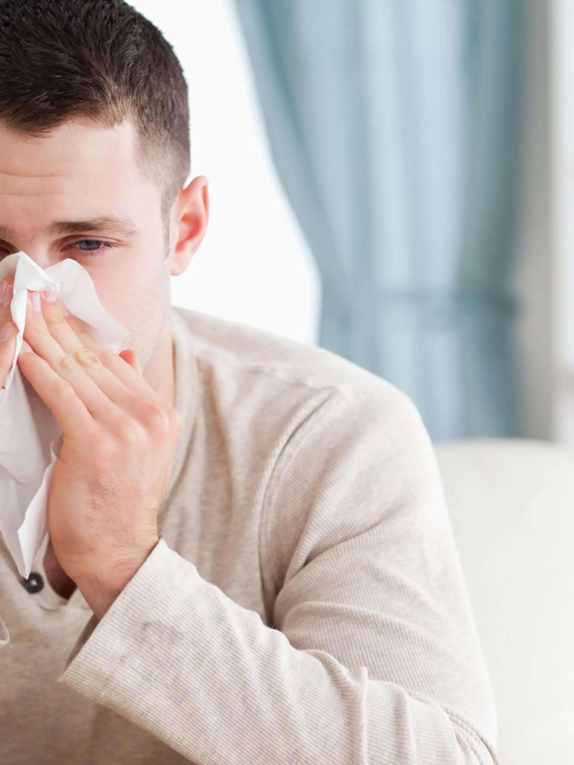Man blowing his nose in his living room