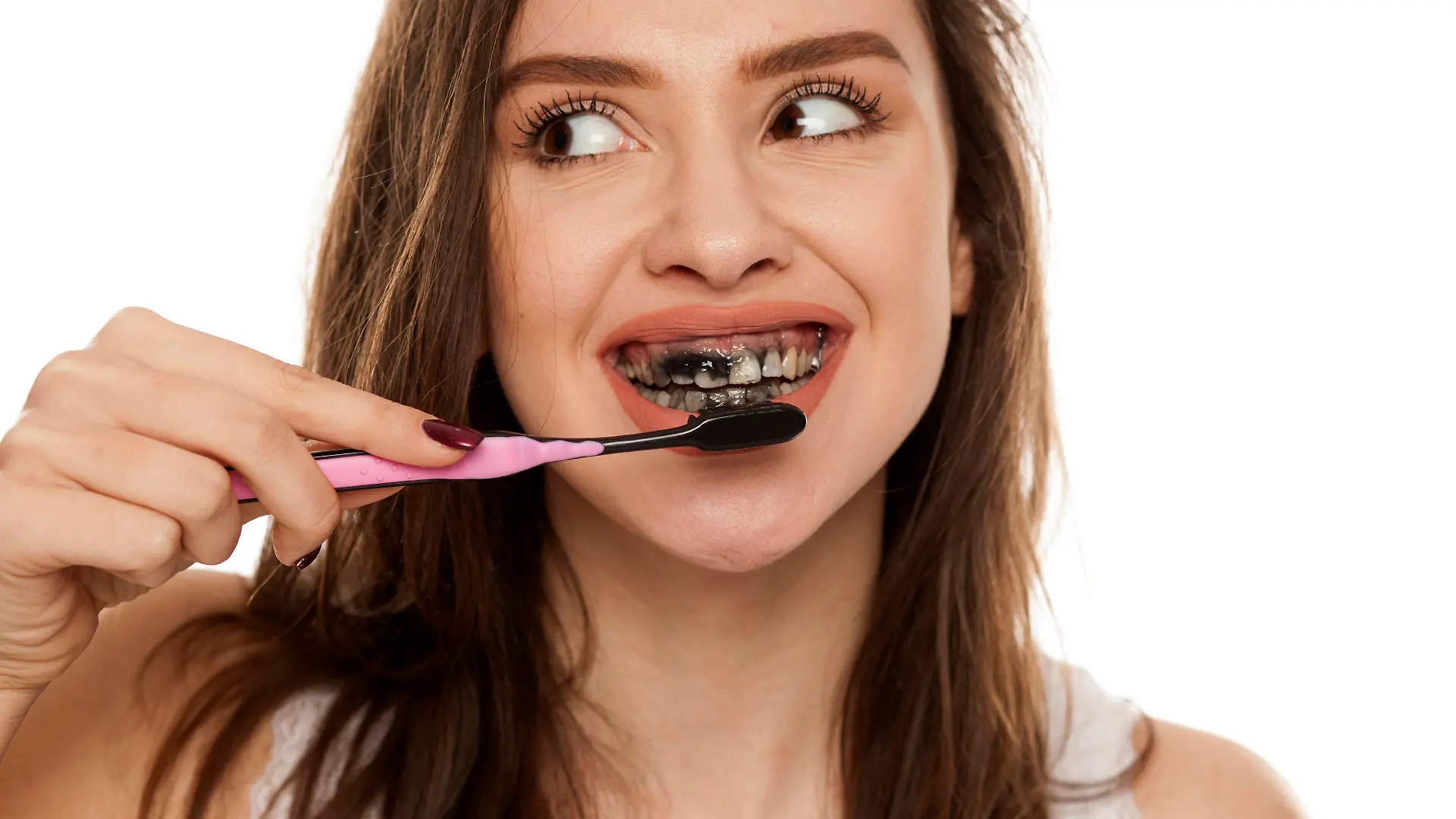 young woman brushing her teeth with a black tooth paste with active charcoal, and black tooth brush on white background, and showing thumbs up