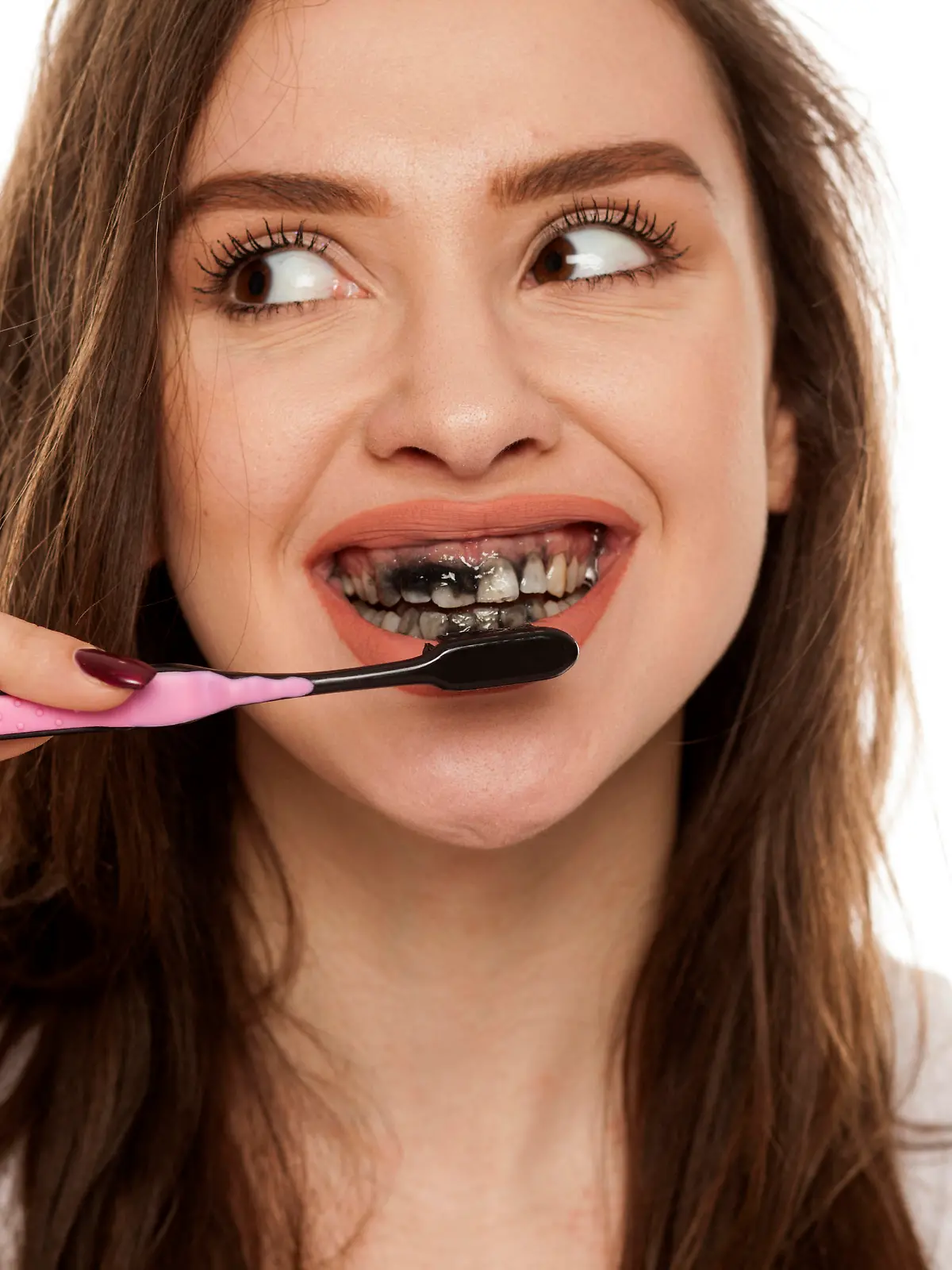 young woman brushing her teeth with a black tooth paste with active charcoal, and black tooth brush on white background, and showing thumbs up