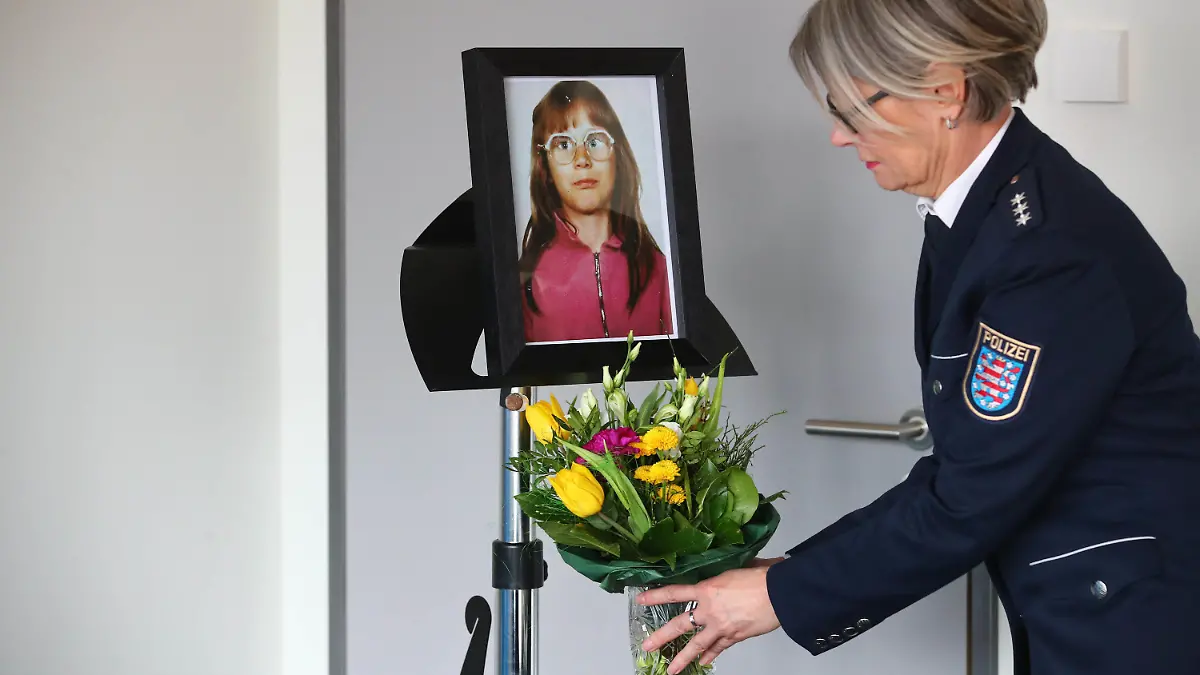 06.03.2018, Thüringen, Jena: Eine Polizeibeamtin der Polizei Jena stellt einen Blumenstrauss unter das Foto der ermordeten Stephanie Drews vor einer Pressekonferenz der Polizei Jena. Grund ist die Klärung des Falles der toten Stephanie Drews aus dem Jahre 1991. Im Zuge der Aufklärung wurde ein Tatverdächtiger Mann festgenommen. Der Fall ist einer und der älteste der drei ungeklärten Kindermorde in Jena und Weimar, mit denen sich die Soko "Altfälle" seit November 2016 beschäftigt. Foto: Bodo Schackow/dpa-Zentralbild/dpa +++ dpa-Bildfunk +++