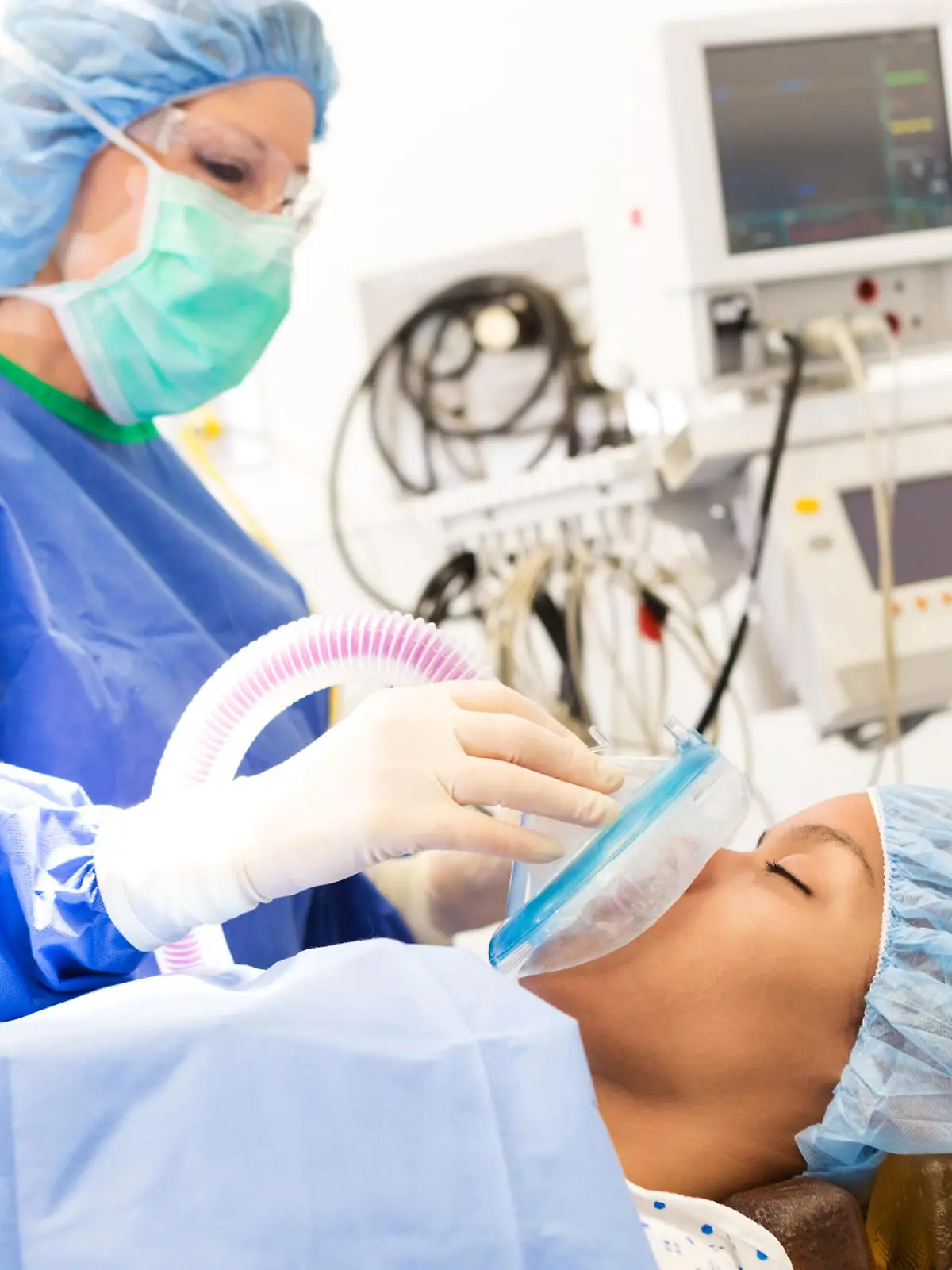 Young adult African American female patient is being sedated while laying on operating table. Senior adult Caucasian female anesthesiologist is using medical equipment to sedate patient.