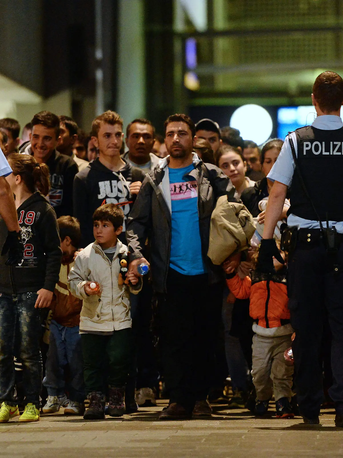 ARCHIV - Flüchtlinge kommen am 12.09.2015 mit einem Zug aus Budapest am Hauptbahnhof in München (Bayern) an und gehen von Polizisten begleitet durch den Bahnhof. Die Flüchtlingskrise stellt die Polizei vor enorme Herausforderungen. Die Überstunden gehen in die Millionen. Nicht alle anderen Aufgaben können wie bisher erfüllt werden. Foto: Andreas Gebert/dpa (zu dpa-Umfrage: "Belastung an vielen Fronten: Polizei durch Flüchtlinge im Stress" vom 22.09.2015) +++(c) dpa - Bildfunk+++
