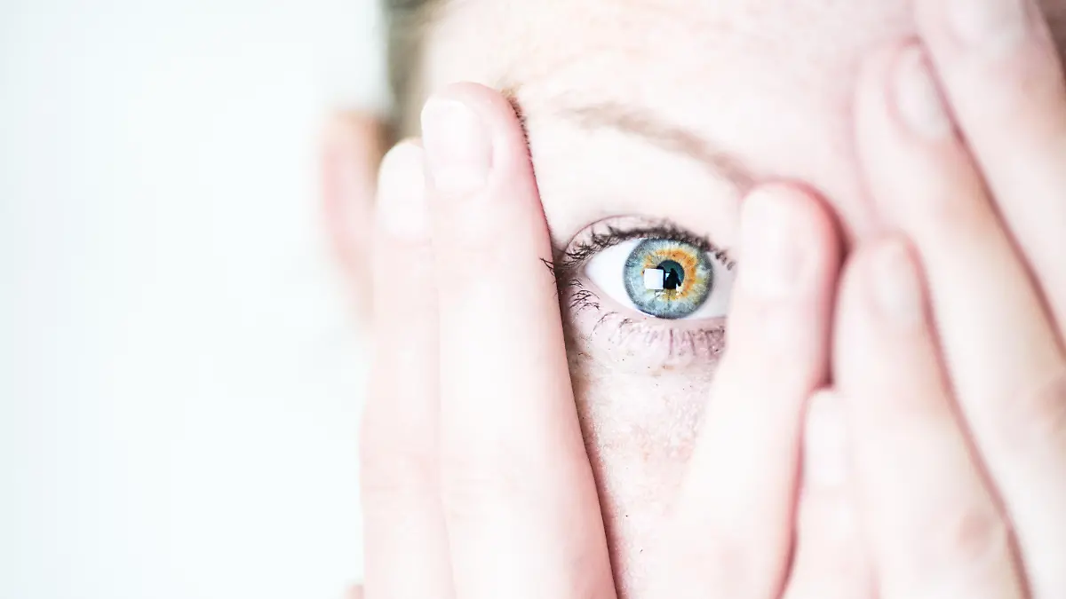 ILLUSTRATION - Eine junge Frau schaut erschrocken zwischen ihren Fingern hervor, die sie sich vor ihr Gesicht haelt (gestellte Szene). Foto: Franziska Gabbert | Verwendung weltweit
