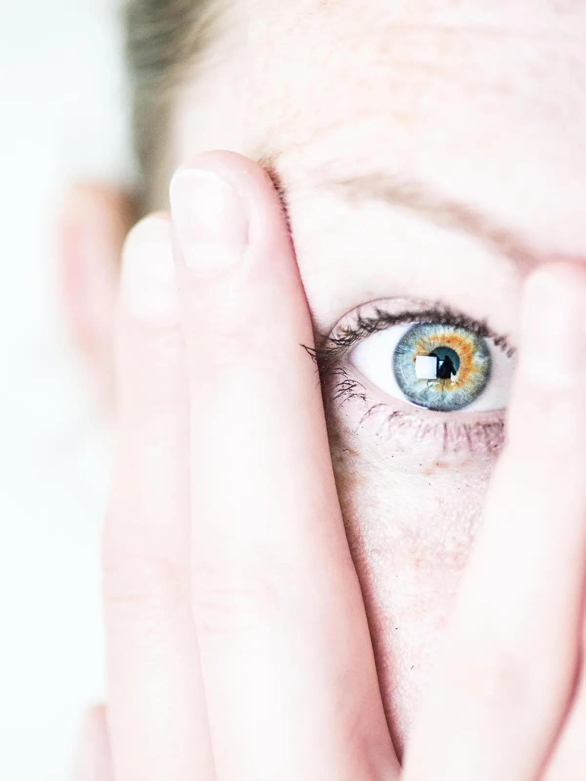 ILLUSTRATION - Eine junge Frau schaut erschrocken zwischen ihren Fingern hervor, die sie sich vor ihr Gesicht haelt (gestellte Szene). Foto: Franziska Gabbert | Verwendung weltweit