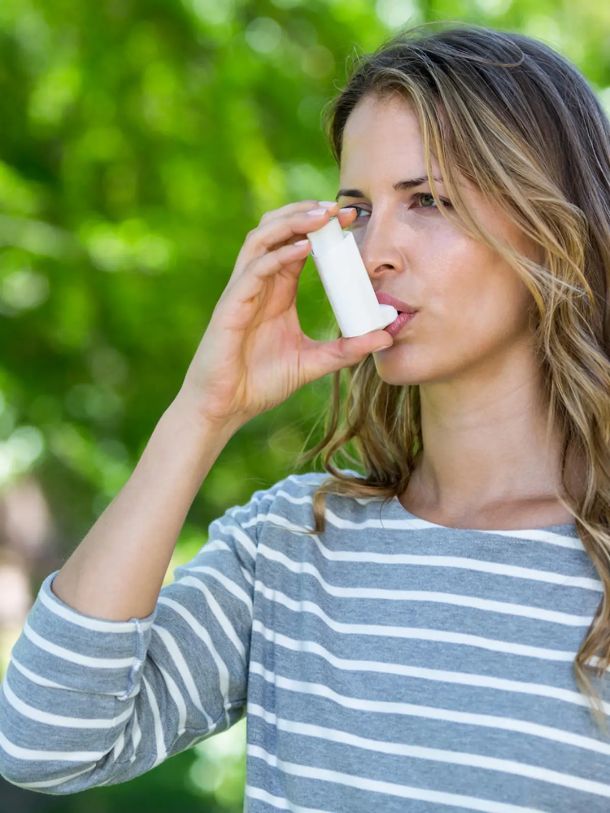 Woman using asthma inhaler in a park