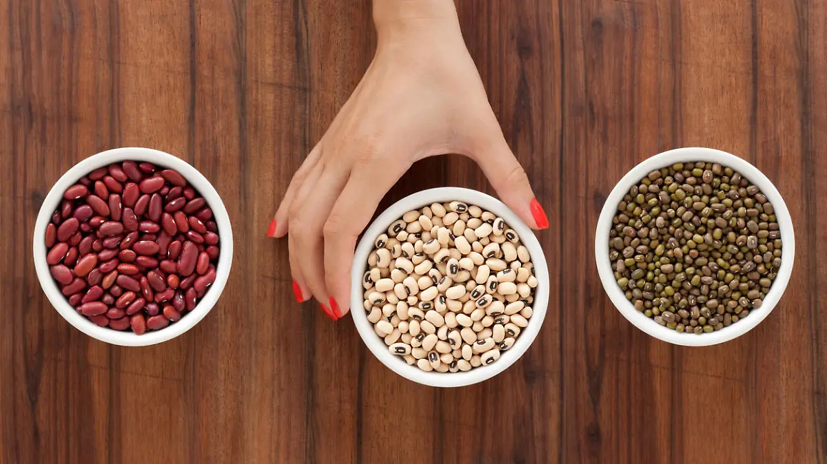 Top view of three bowls containing bean varieties and one woman hand holding the one in the middle