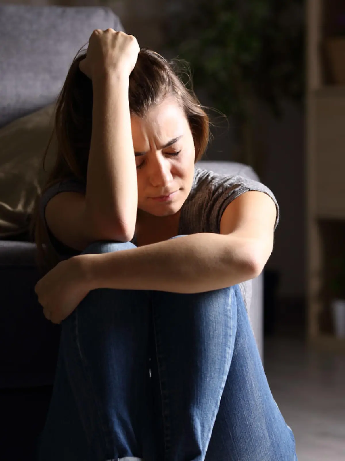 Eine junge Frau sitzt traurig und depressiv auf dem Boden.