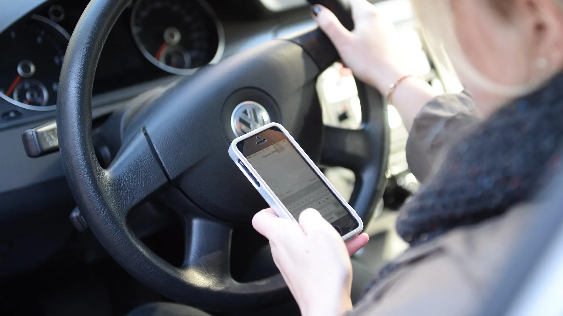 ARCHIV - ILLUSTRATION - Eine Frau sitzt am 02.10.2015 in Düsseldorf (Nordrhein-Westfalen) im Auto am Steuer und liest Nachrichten auf ihrem Smartphone.     (zu dpa «Autofahrer mit Handy am Ohr - die Unsitte greift um sich» vom 10.03.2017) Foto: Monika Skolimowska/dpa +++(c) dpa - Bildfunk+++