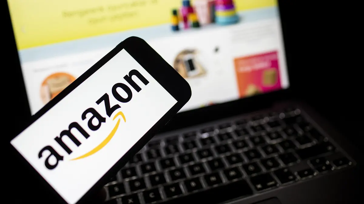 Amazon-Logo auf einem Smartphone, im Hintergrund der Amazon-Onlineshop auf einem Laptop