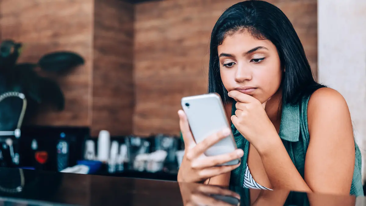 Eine junge Frau schaut genervt auf ihr Handy.