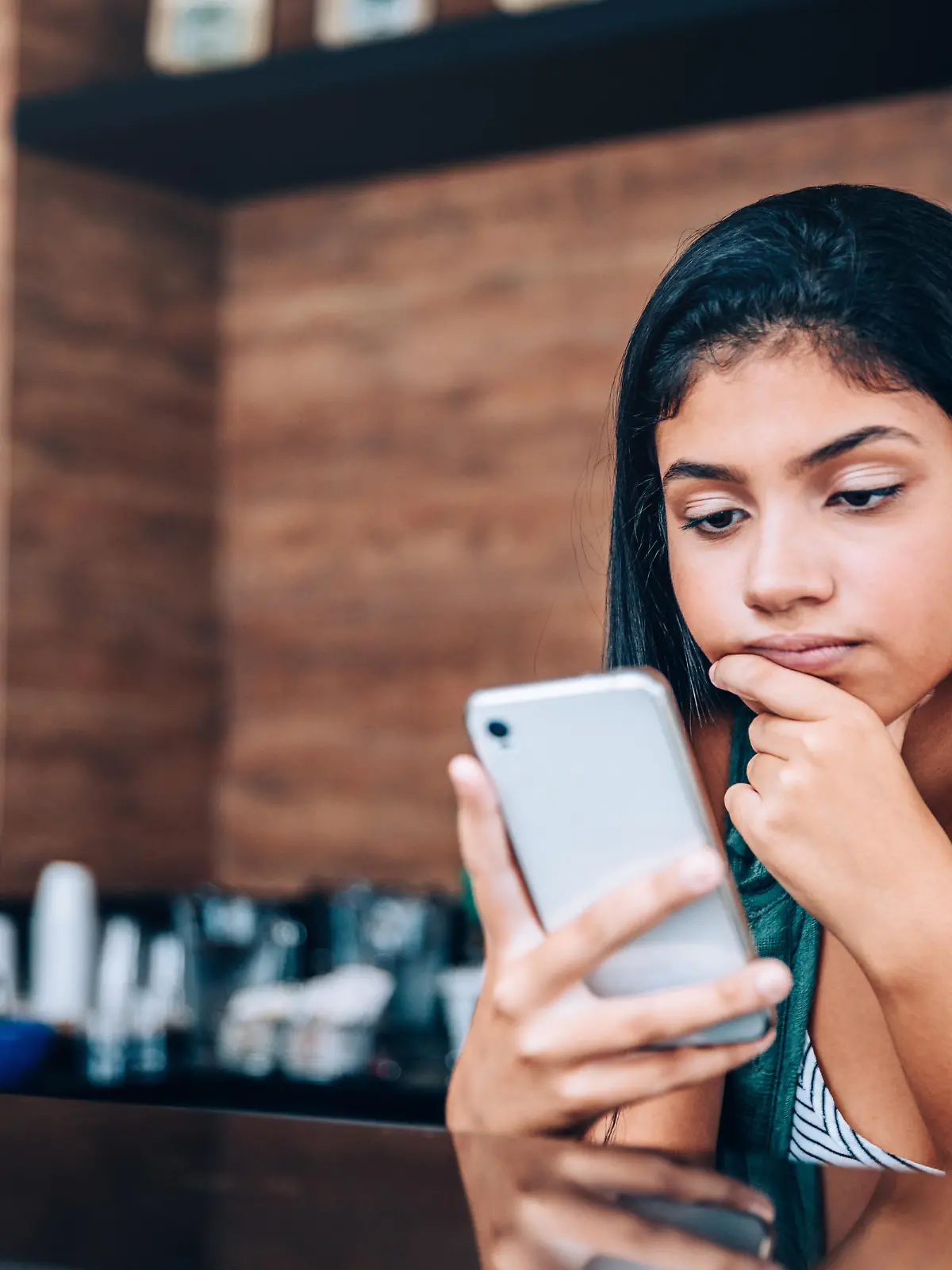Eine junge Frau schaut genervt auf ihr Handy.