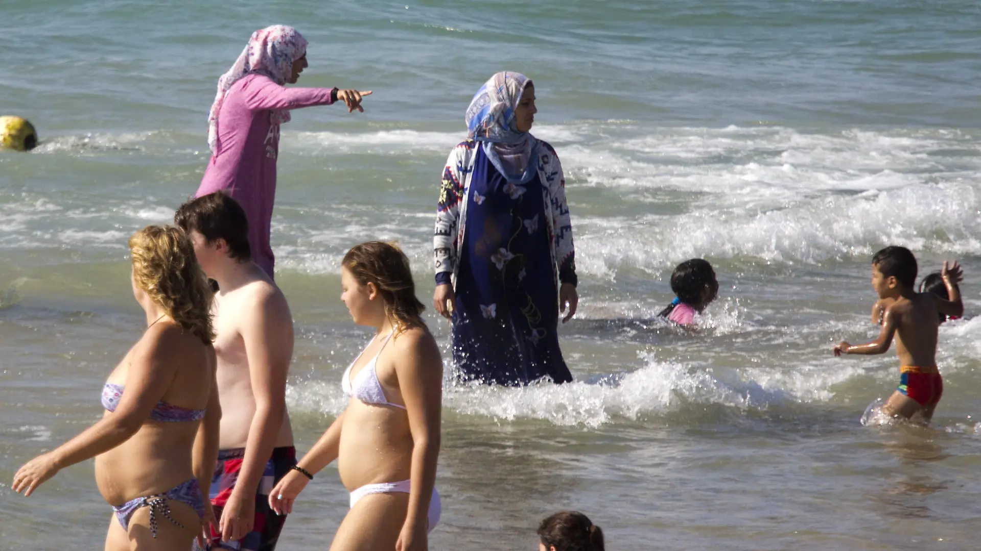 Eine Frau im Burkini badet neben Menschen in Bikini und Badehose.