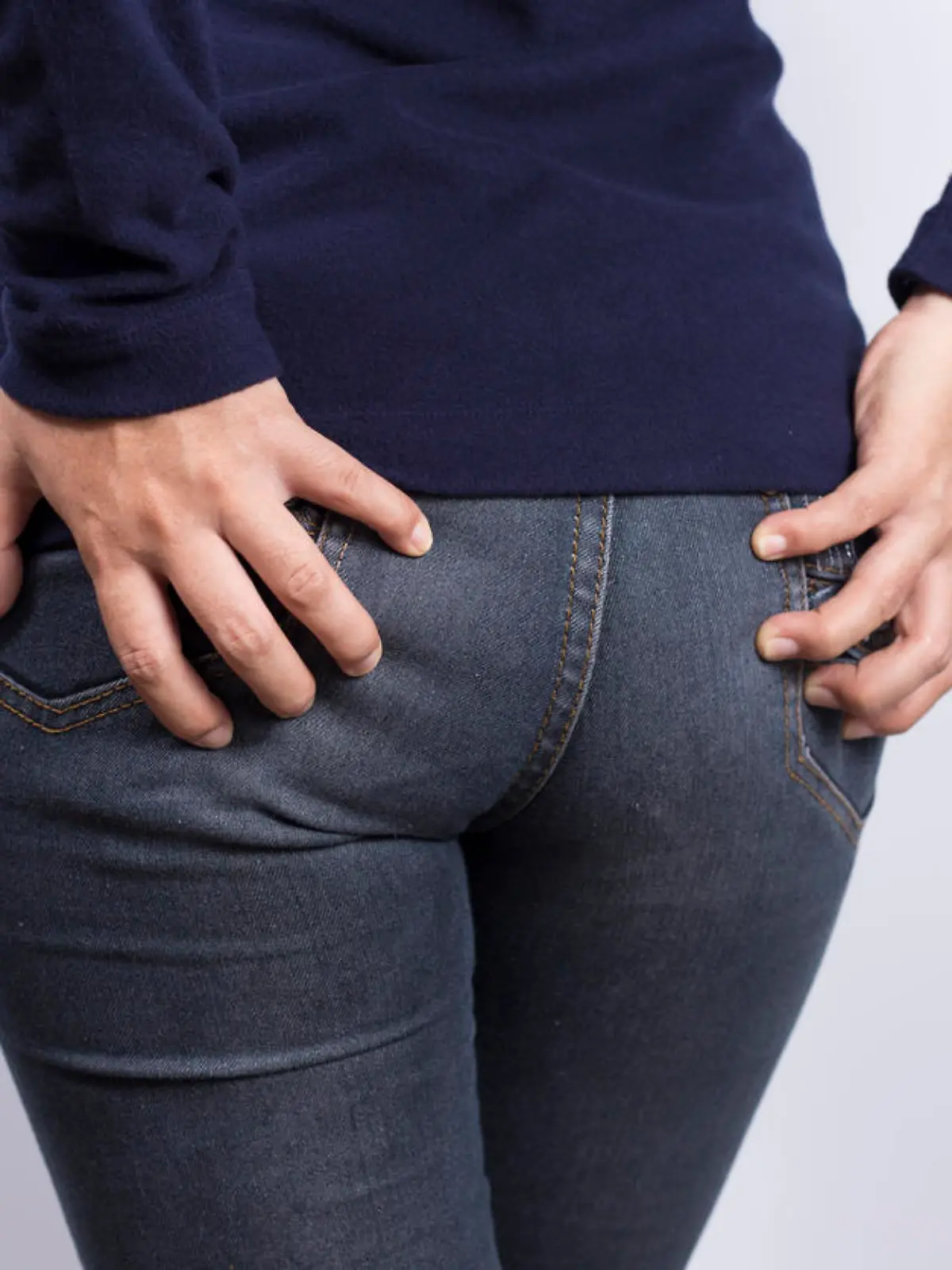 Eine Frau in Jeans hält die Hände an ihrem Gesäß.