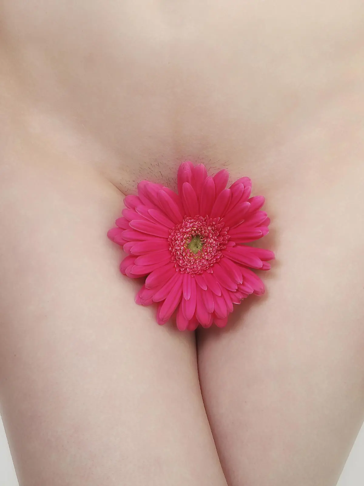 Eine junge Frau bedeckt mit einer Blume ihren Intimbereich.