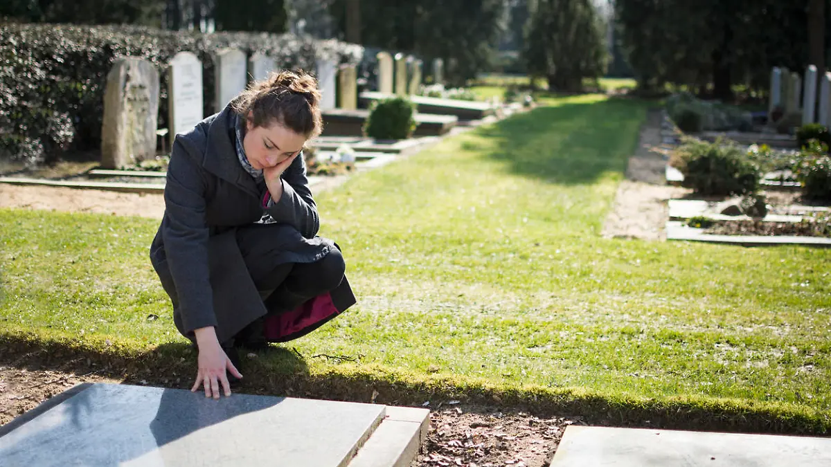 Eine trauernde Frau vor einem Grabstein auf dem Friedhof