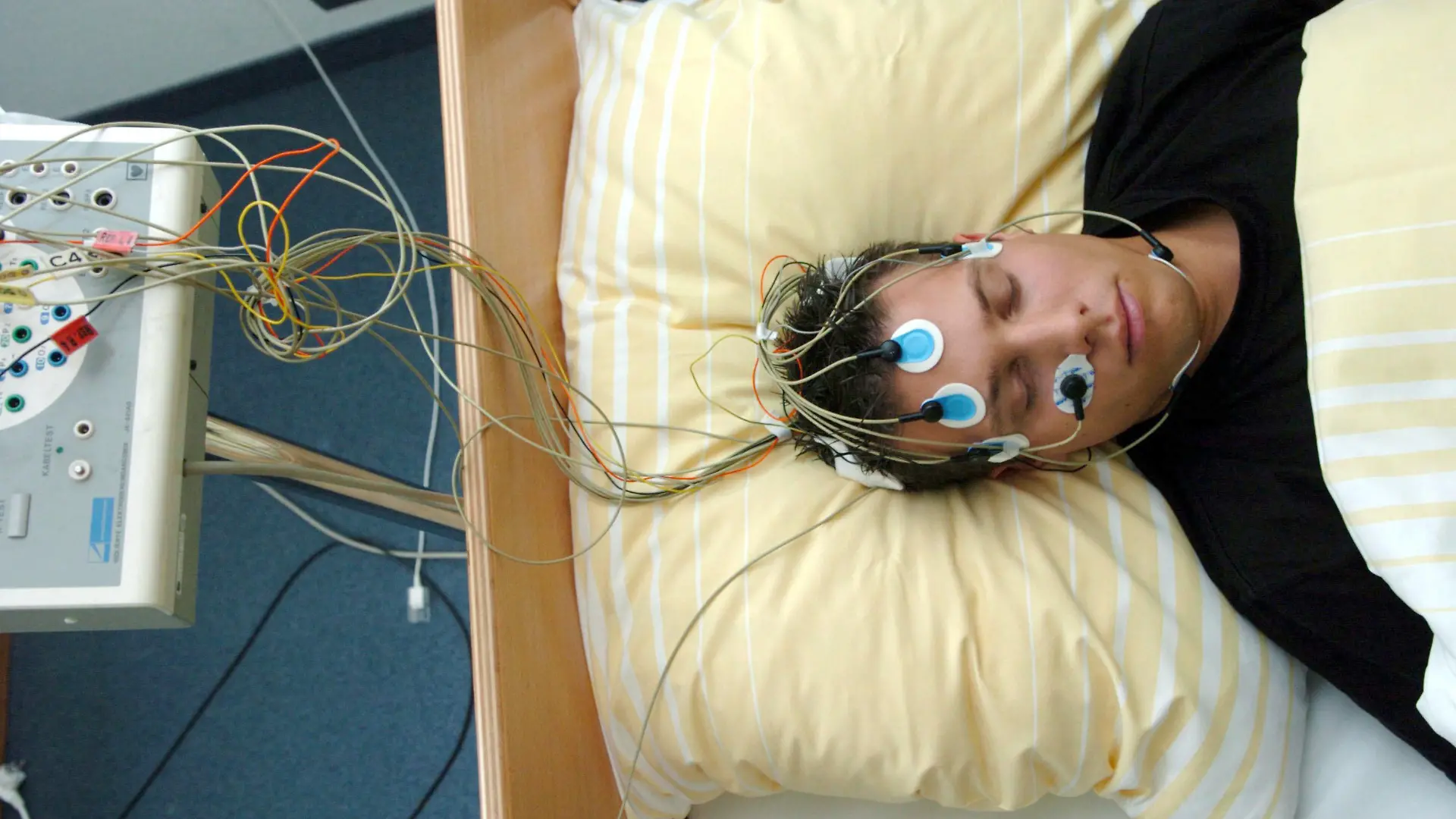 ARCHIV - Ein Patient des Schlaflabors der Universitätsklinik Freiburg liegt, am Kopf mit Elektroden bestückt, in einem Bett der Einrichtung (Archivoto vom 22.09.2004). Kabel leiten die gemessenen Hirnströme an ein Aufzeichnungsgerät weiter. Laut Deutscher Gesellschaft für Schlafforschung und Schlafmedizin leiden rund fünf Prozent der Bevölkerung unter ernsten und behandlungsbdürftigen Schlafstörungen. Foto: Rolf Haid dpa/lnw (zu lnw-KORR: " Wenn Schlaf zum Albtraum wird" vom 10.07.2006) +++(c) dpa - Bildfunk+++