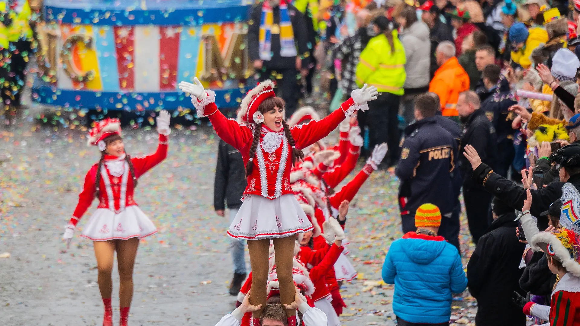 ARCHIV - 24.02.2020, Rheinland-Pfalz, Mainz: Ein Tanzmariechen des Mainzer Narren-Clubs (MNC) wird auf den Schultern getragen. Polizisten sichern den Rosenmontagszug, der zuletzt 2020 stattfand. In diesem Jahr bereiten Auflagen für Sicherheitsvorkehrungen den Veranstaltern Sorgen. (zu dpa: ««Fastnacht ist eine ernste Sache» - Streit um die Sicherheit) Foto: Andreas Arnold/dpa +++ dpa-Bildfunk +++