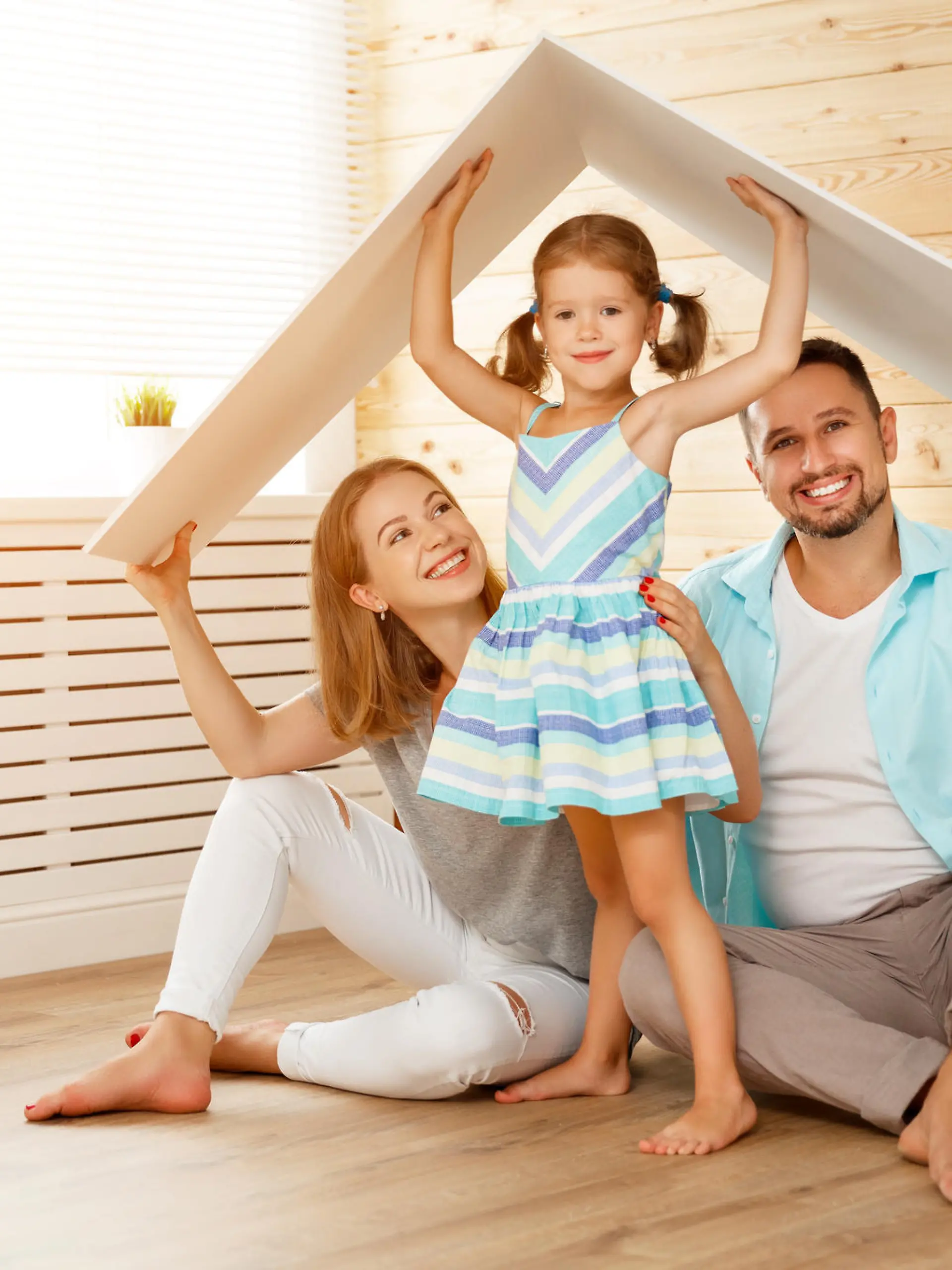 Familie mit einem Kind in neuem Zuhause mit symbolischem Dach über dem Kopf.