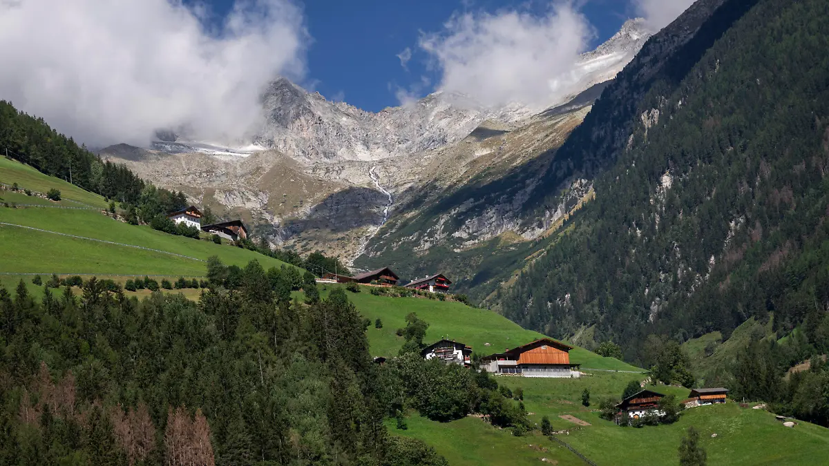 Malerisch schmiegen sich Häuser an diesen Berg bei St. Johann im Ahrntal (Südtirol/Italien). im Hintergrund verhüllen Wolken die Gipfel der Zillertaler Alpen aufgf der österreichischen Seite der Alpen. (02.09.2022)