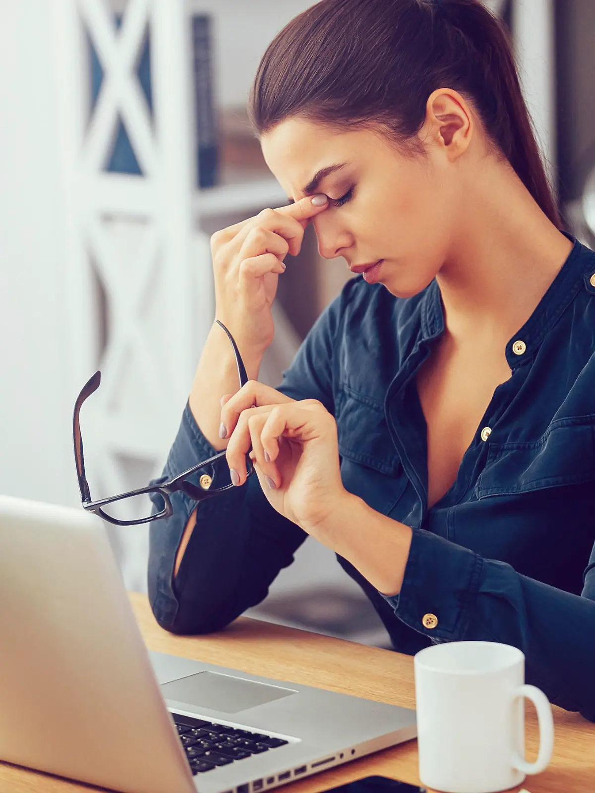 Frustrated young woman keeping eyes closed and massaging nose while sitting at her working place in office