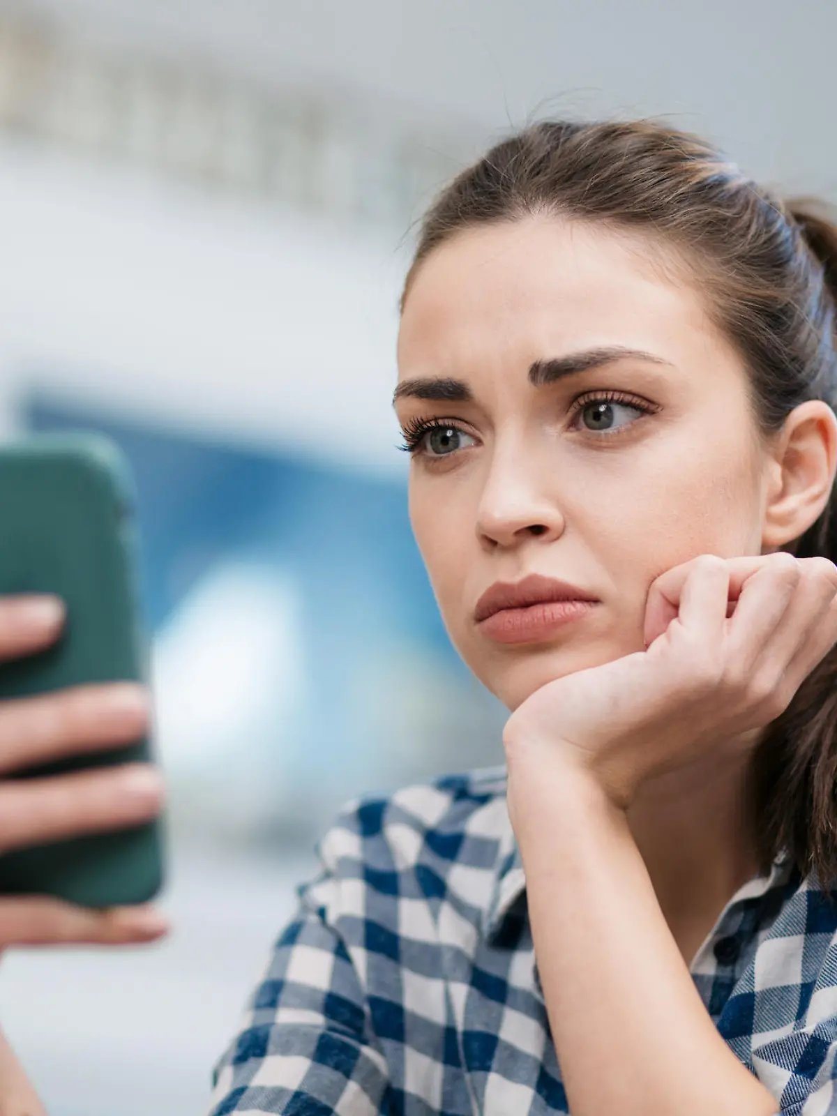 Close up of a depressed Caucasian young woman sitting at home, reading some bad news on her smart phone, feeling sad and worried