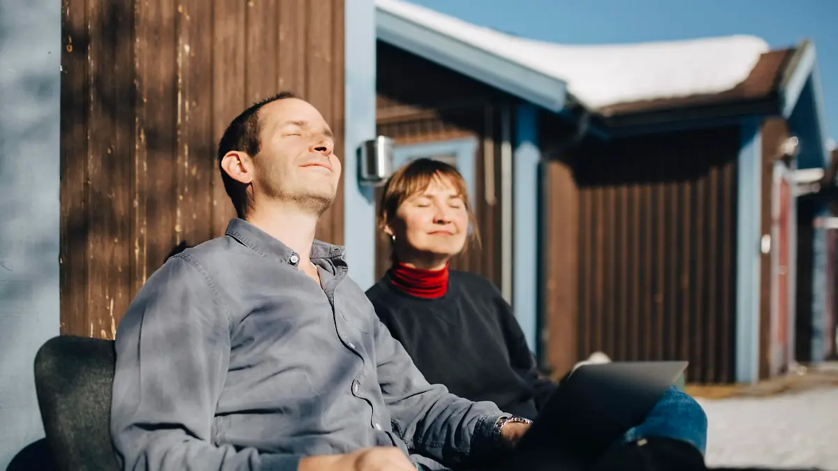 IMAGO Creative: Jahreszeit Frühling, Frühlingsanfang am 20. März Male and female professionals sitting with eyes closed against vacation home during sunny day Sweden, Kiruna, model released Copyright: xMaskotx , MA86957