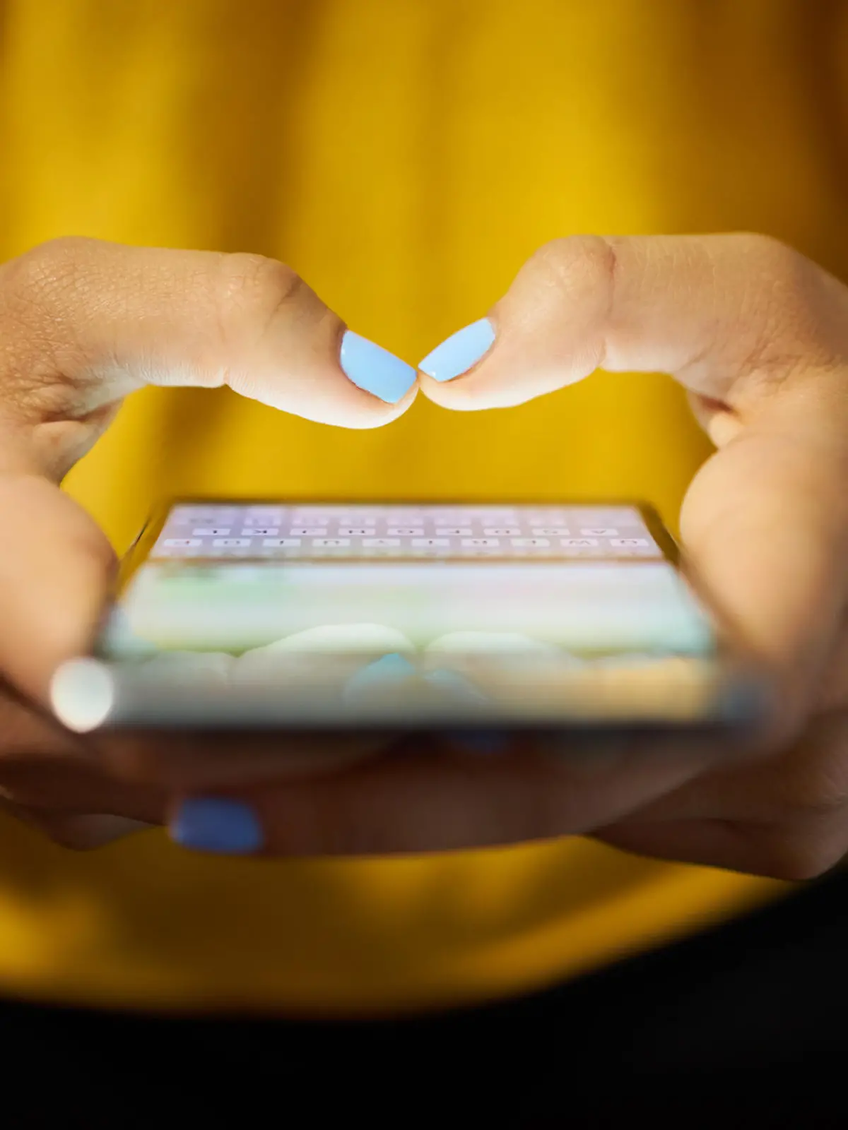 Young woman using cell phone to send text message on social network at night. Closeup of hands with computer laptop in background