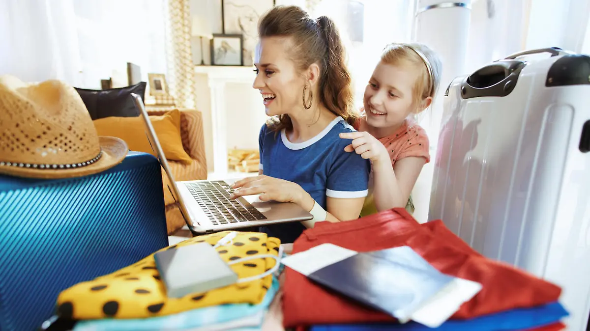 smiling modern mother and child travellers at modern home in sunny summer day buying plane tickets.