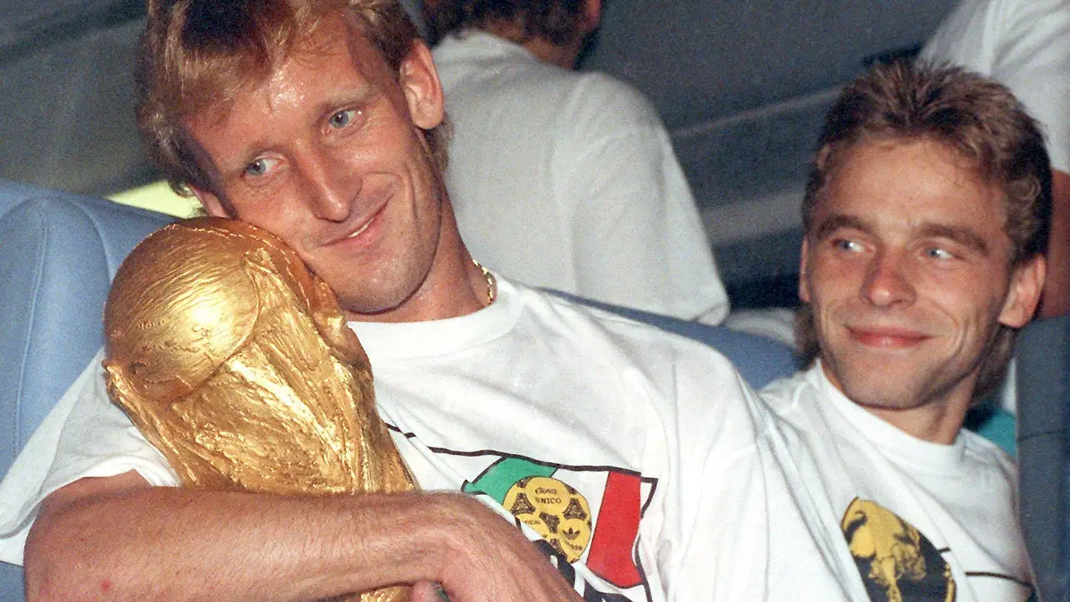 ARCHIV - 09.07.1990, Frankfurt/Main: Andreas Brehme (l), damaliger deutscher Fußballnationalspieler nimm den WM-Pokal in den Arm und sein Teamgefährte Thomas Häßler schaut lächelnd zu. (zu dpa: «Von Illgner bis Völler: Zwölf Helden in der magischen Nacht von Rom») Foto: picture alliance / Frank Kleefeldt/dpa +++ dpa-Bildfunk +++