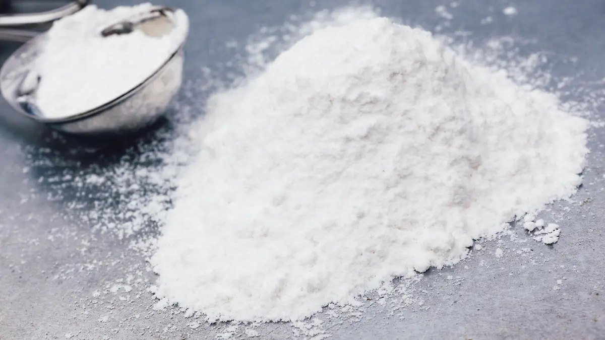 Heap of baking soda with measuring spoon on a metal baking tray.