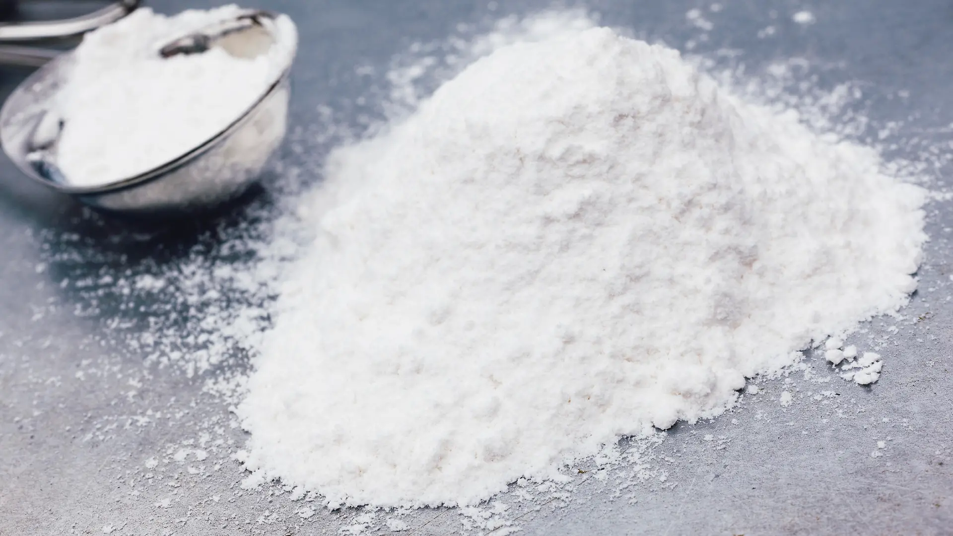 Heap of baking soda with measuring spoon on a metal baking tray.