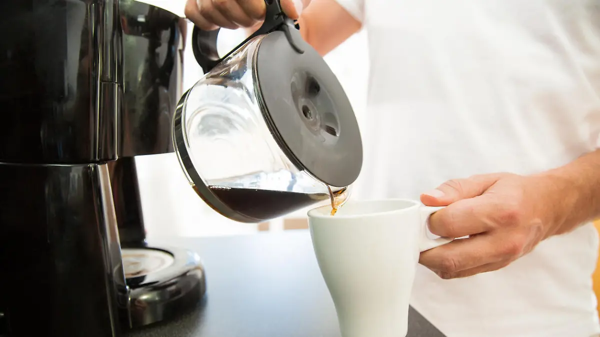Ein Mann gießt sich am Morgen eine Tasse Kaffee aus einer Filtermaschine ein.