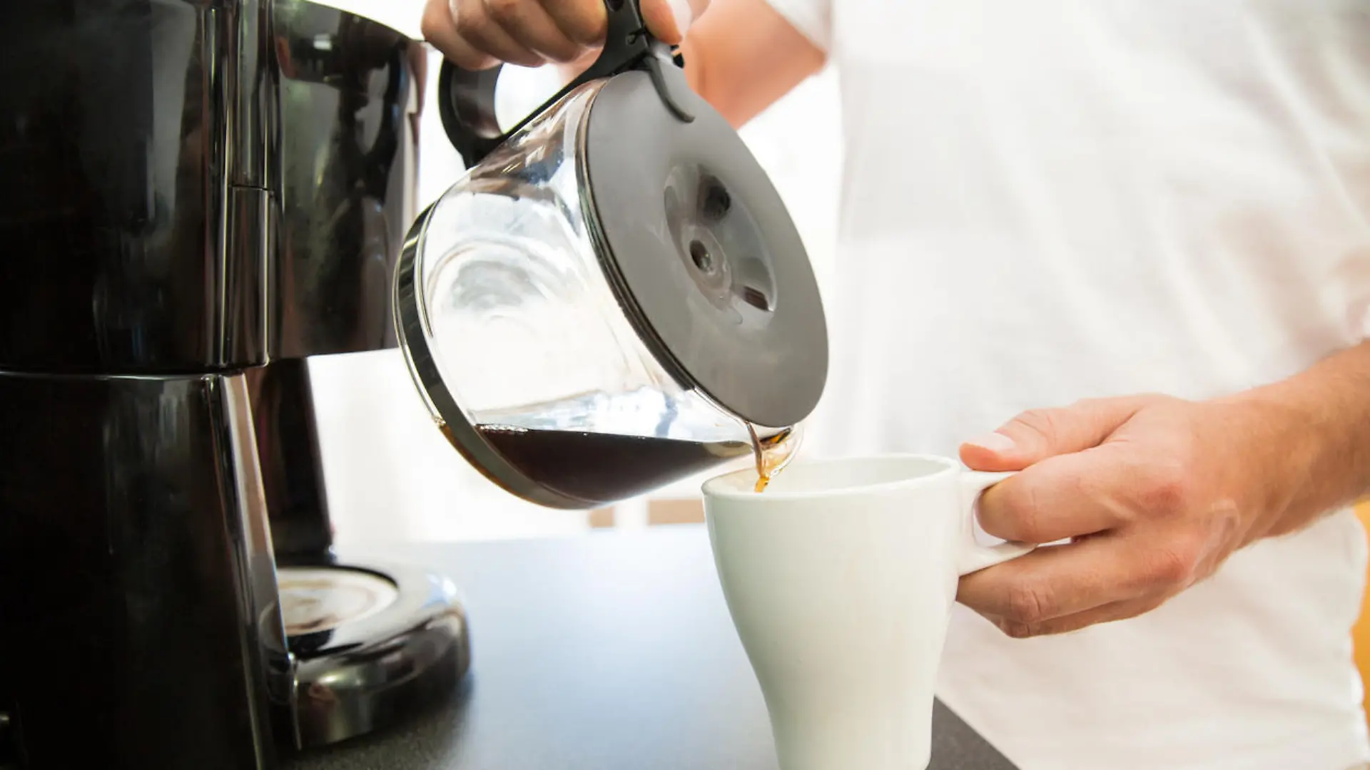 Ein Mann gießt sich am Morgen eine Tasse Kaffee aus einer Filtermaschine ein.
